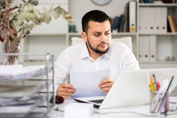 Fototapeta premium Serious male office worker sitting at desk and doing paperwork.