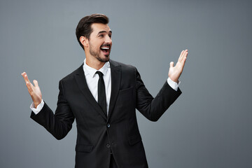 Man businessman surprised smile with teeth and raised his hands up happy in a business suit on a gray background with a brunette beard