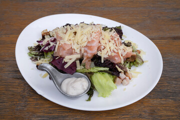 Closeup view of a Caesar salad with lettuce, parmesan cheese, bread croutons, salmon, bacon and Caesar dressing, in a white plate on the wooden table.	
