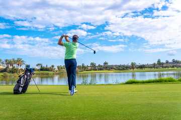 Man playing golf at golf club by a lake, hitting the ball © unai