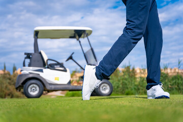 Golf driver stick preparing to hit the ball. Unrecognizable man playing golf next to a buggy car