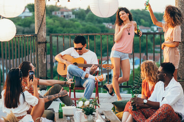 A man plays guitar to his friends at the rooftop party.