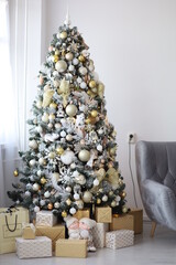 a New Year's Christmas tree is tall decorated with white and gold toys with a lot of gifts under it near the sofa in a cozy room