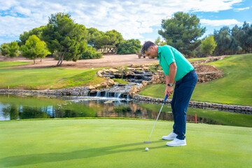Fototapeta premium Playing golf at golf club by a lake on the green, hitting the ball with the putter