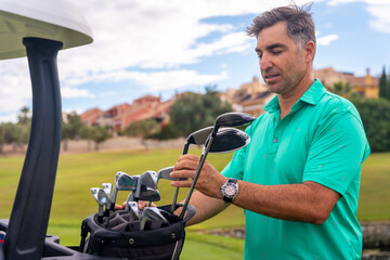 Man playing golf at golf club, checking golf clubs before hitting the ball