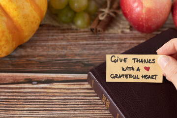 Hand holding a handwritten thanksgiving note to give thanks with a grateful heart with closed Holy Bible Book and fresh autumn fruit on wooden background with copy space. A closeup. Christian concept. - obrazy, fototapety, plakaty