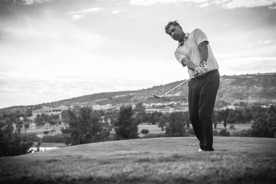 Handsome young man playing golf hitting the ball onto the green. black and white photo