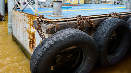 Fototapeta premium car tire with a metal chain on a old concrete sea pier,old truck tires at the pier.tire bumpers