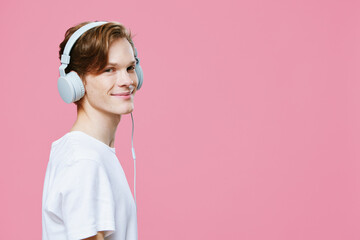 portrait of a cute red-haired guy in a t-shirt listening to music in bright headphones smiling...