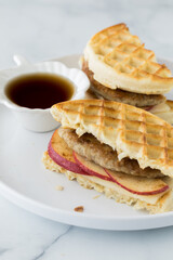 A homemade waffle and sausage sandwich served with maple syrup for dipping.