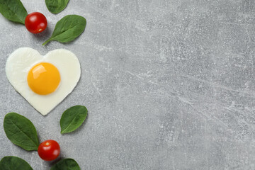 Heart shaped fried egg, tomatoes and spinach on light grey table, flat lay. Space for text