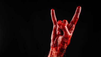 A man's hand covered in blood shows a goat sign on a black background.