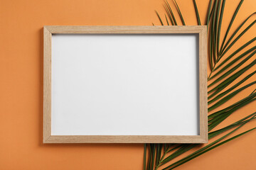 Blank photo frame and tropical leaf on orange background, flat lay