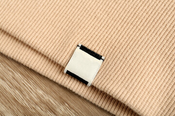 Beige apparel with blank clothing label on wooden table, top view