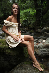 Beautiful young woman sitting on rock near mountain river in forest