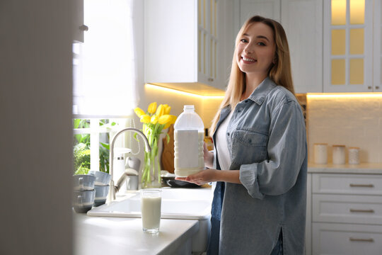 Young woman with gallon bottle of milk and glass at white countertop in kitchen