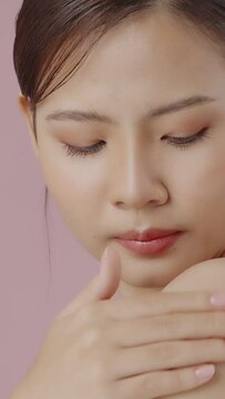 Vertical young beautiful Asian woman applying moisturizer cream on her shoulder gently on pink background.