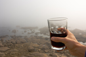 Woman's hand with glass glass in nature, Fog in the distance ocean and shore of stones, atmospheric and fresh