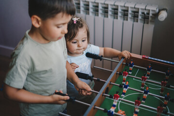 Happy little kids playing table soccer at home, having fun with board football, indoors. Corona...