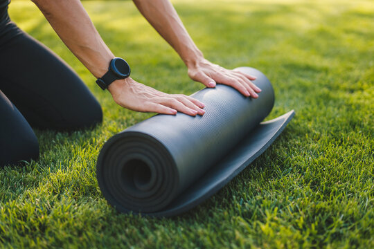 Cropped image of female hands folding exercise mat before working out in the park. Equipment for fitness. Healthy active lifestyle. Healthy activity. Training