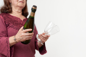 Hispanic mature woman holding a bottle of champagne or cider and a pair of glasses. Concept of celebratory toast. Selective focus composition with copy space.
