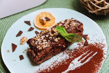 Sweet breakfast with chocolate honey biscuit cake with sour and butter cream and walnuts, a slice of dried orange and decorated with mint leaf and cocoa powder