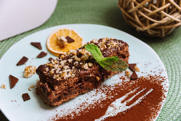 Fototapeta na wymiar Sweet breakfast with chocolate honey biscuit cake with sour and butter cream and walnuts, a slice of dried orange and decorated with mint leaf and cocoa powder