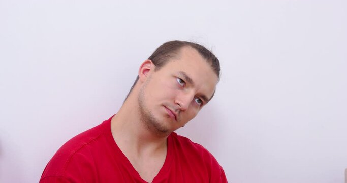 Young guy in a red t-shirt and with a stylish hairstyle does neck exercises, front view. Necessary activity and exercises for joints and muscles with a sedentary lifestyle.
