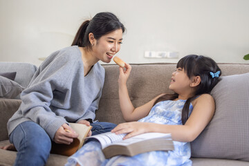 Obraz na płótnie Canvas Happy asian mom holding her daughter playing and reading E-book on sofa at home.little girl hugging her mother smile and love having fun at home.Mother day concept