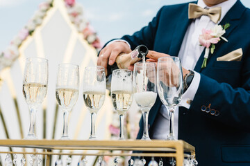 The waiter pours the champagne into the glasses from the bottle on party. Catering service, banquet. official event.