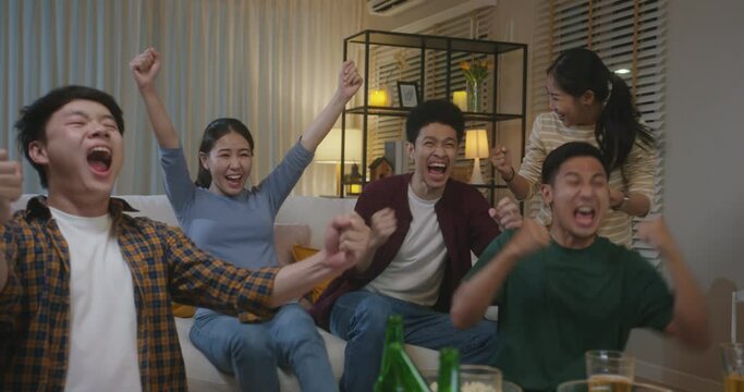 Group of young adult friend man and woman asia people sit at sofa couch joy night party fun game match world cup live TV at home eat snack bowl drink beer bottle glass jump mad happy win exult face