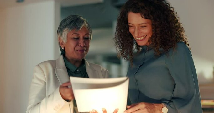 Teamwork, paper and documents with business women laughing and working late on a report or proposal in an office. Management, contract and senior executive with humour planning and celebrating vision