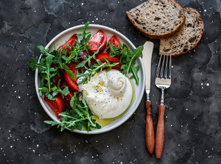Delicious Italian style salad - fresh burrata, arugula and tomatoes on a dark background, top view