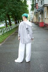 A woman with green hair in white clothes and with an umbrella walks down the street after the rain