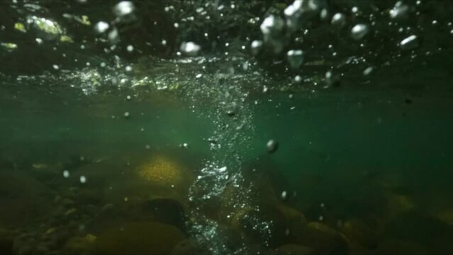 Slow motion underwater shot of a stone falling into a river