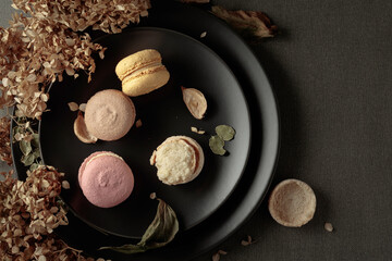 Delicious sweet colorful macaroons with dried flowers on a black plate.