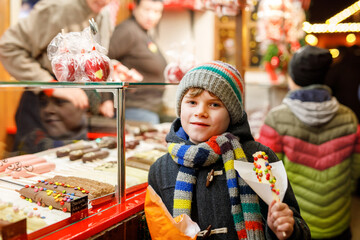 Little kid boy, cute child eating bananas covered with chocolate, marshmellows and colorful...