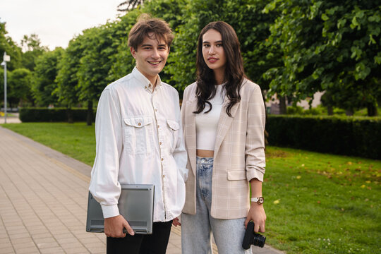 Shot of young happy couple with photo camera and laptop walking in summer park.