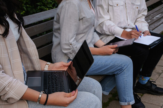 Shot of group of three students together in park with laptop and tablet sitting on bench.