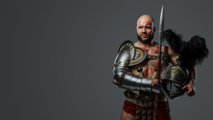 Portrait of handsome gladiator with muscular build holding long spear and plumed helmet.