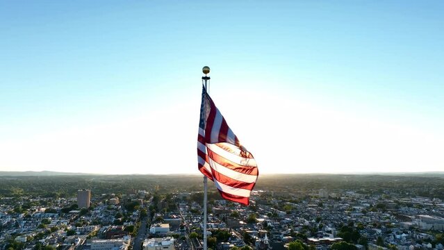 American flag waves in wind. American city and suburb view. Cinematic aerial shot.