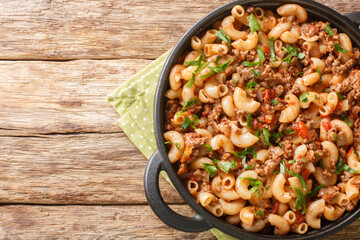 Hamburger Macaroni with with vegetables and cheese closeup in the pan on the wooden table. Horizontal top view from above