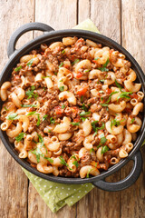 Comfort food ground beef cooked with onions, tomato sauce, and macaroni closeup in the pan on the wooden table. Vertical top view from above