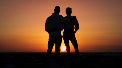 Kobieta i mężczyzna przytuleni na tle zachodzącego słońca - obrazy, fototapety, plakaty