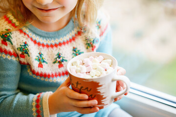 Closeup of little preschool girl holding cup with hot chocolate with marhsmallows. Happy child...