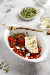 Baked mini tomatoes and Feta cheese with oil and thyme in white dish. Diet dinner idea. Baked feta pasta.