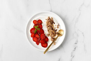 Delicious Breakfast with Yogurt,  strawberry and granola in white plate.  Creamy dairy product. Top view, marble background.