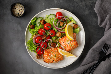 Salmon fish fillet and fresh green vegetable salad with lettuce, tomatoes, onion, mushrooms. Top view. Copy space.