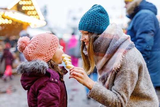 Young mother and daughter eating white chocolate covered fruits on skewer on traditional German Christmas market