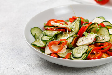 Healthy salad with sliced cucumbers, feta cheese, sweet peppers in a white plate. Fresh green snack. Keto diet. Vegetarian food. Copy space, place for text.